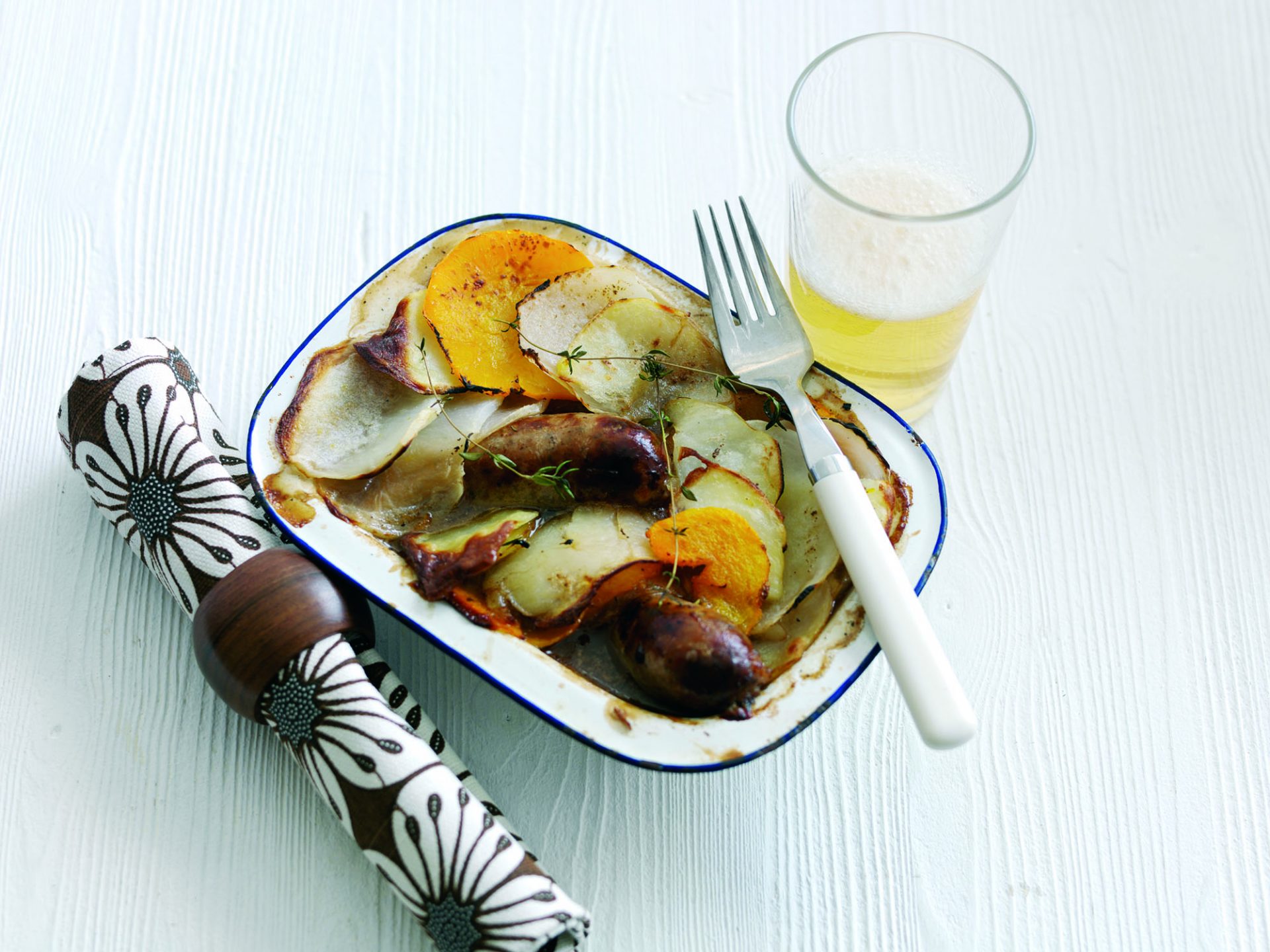 Single portion lancashire hotpot served in a baking dish with fork and glass on side.