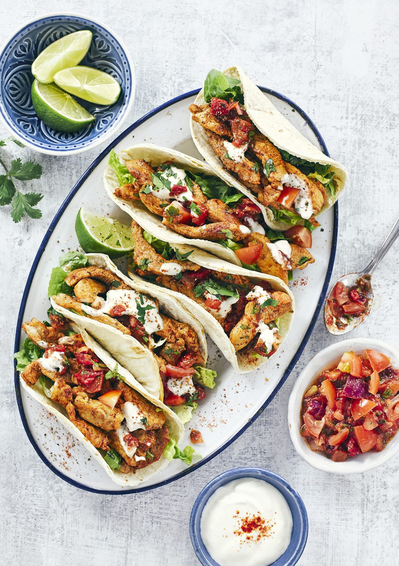 White serving platter with soft tortilla tacos filled with pork.