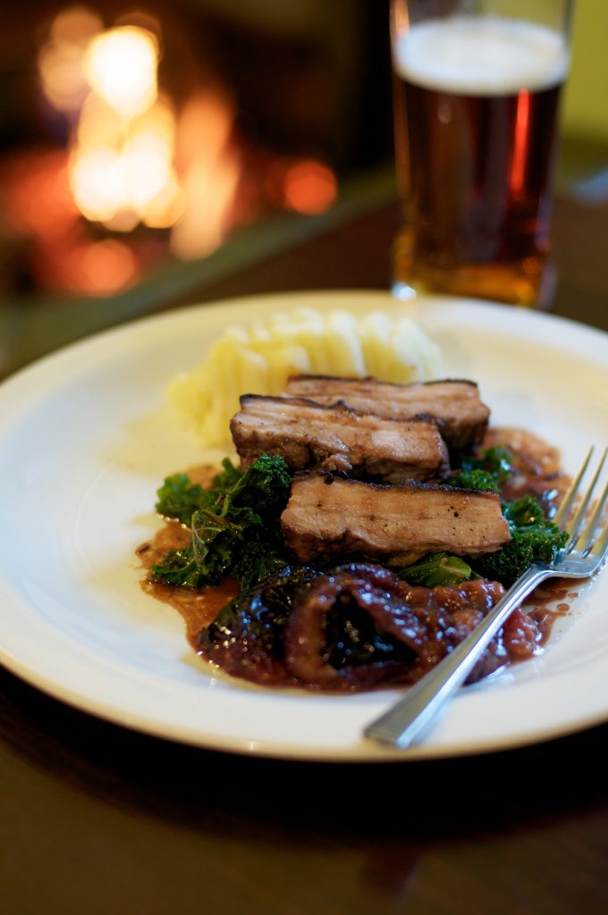 Pork belly with plums, mash and greens on a plate with a fork