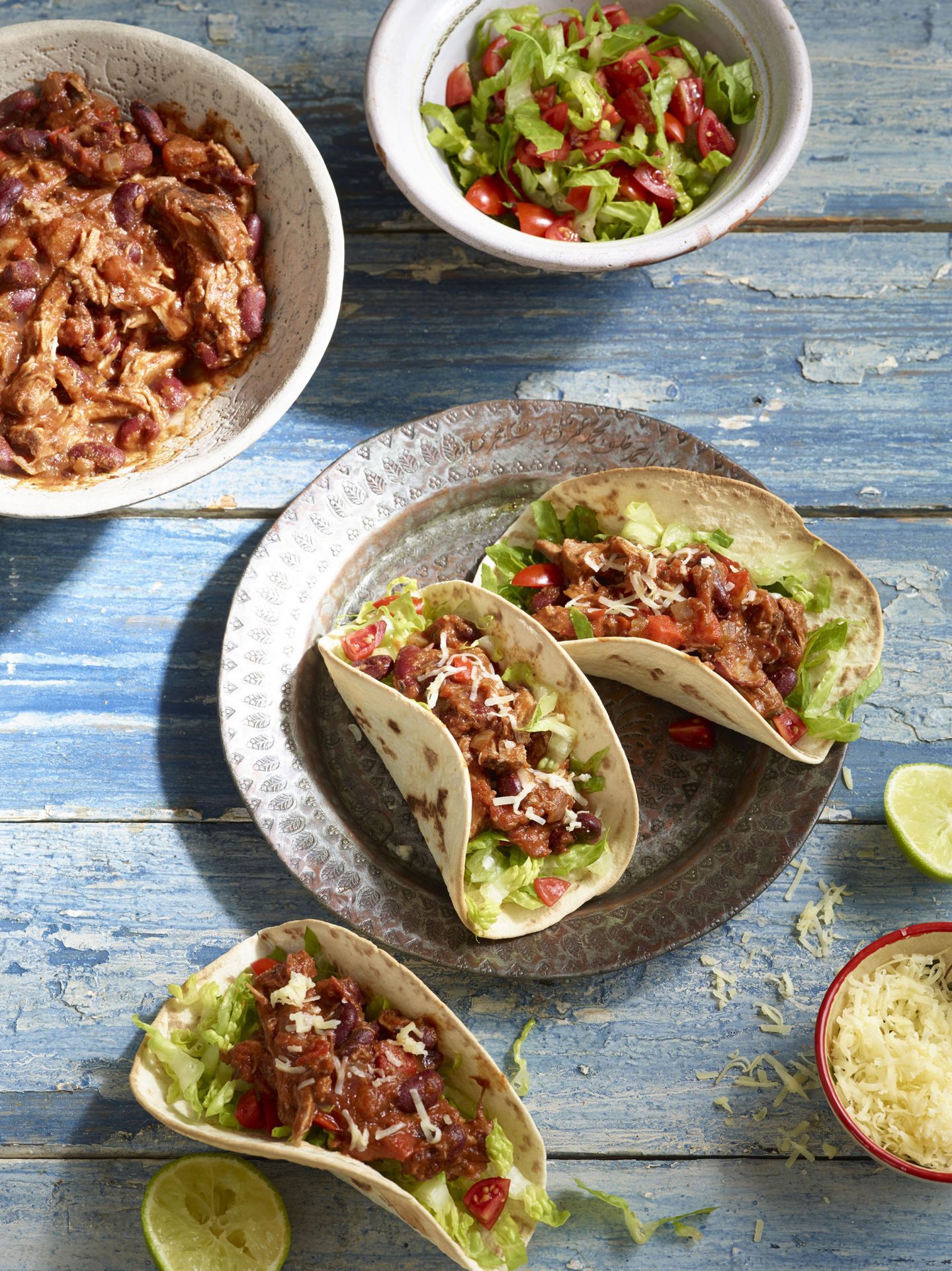 Two soft shell tacos filled with pulled pork chilli and lettuce, served on a metal plate