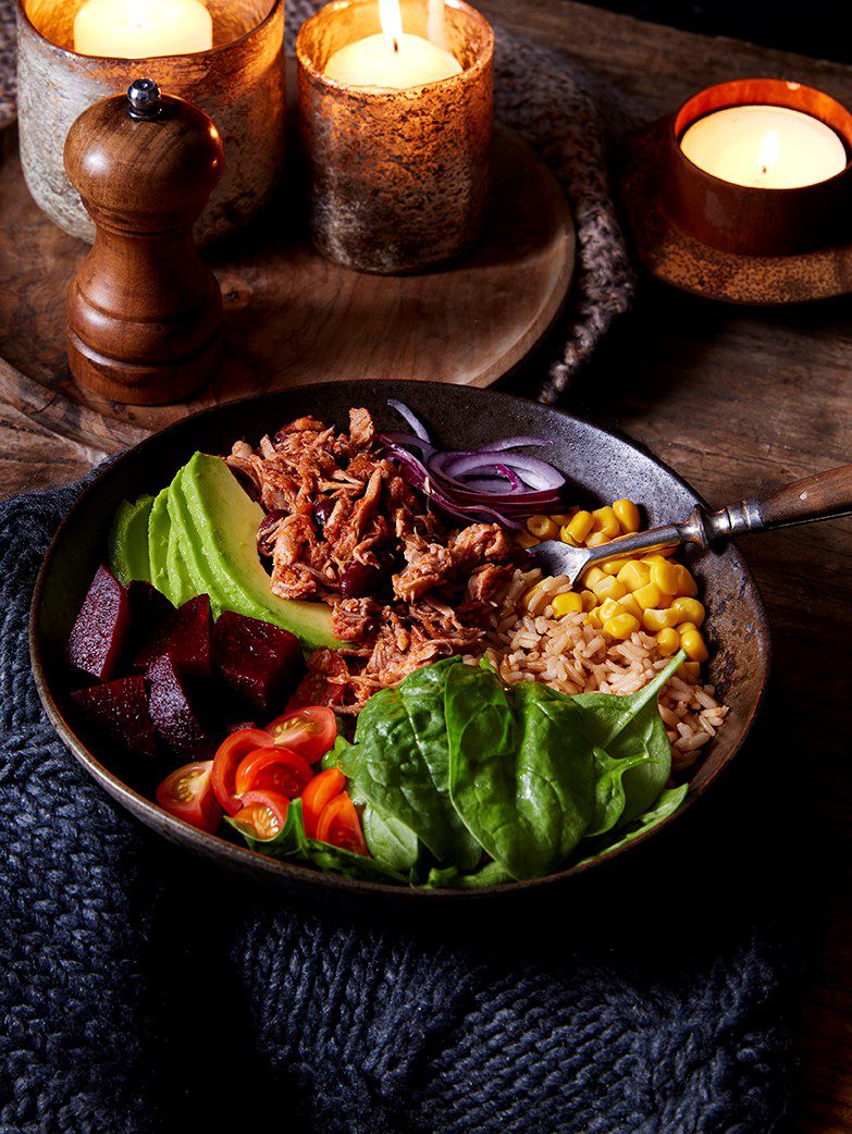 Pulled pork chilli con carne buddha bowl served in a black bowl with fork in