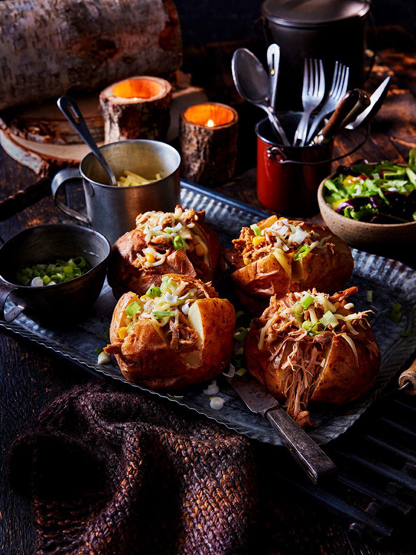 Four pulled pork loaded jacket potatoes on a black platter