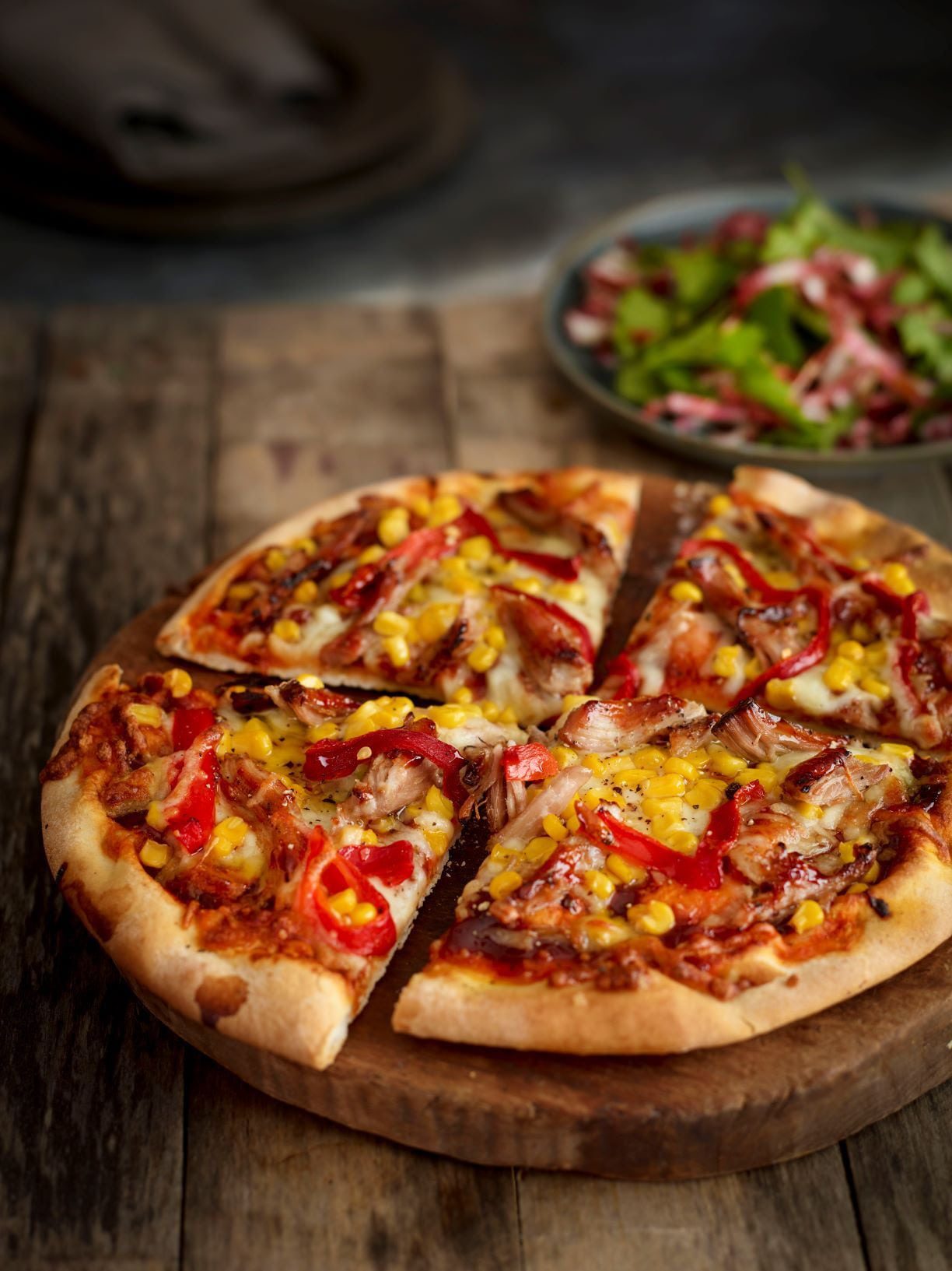 Pulled pork, pepper and sweetcorn topped pizza on a wooden board