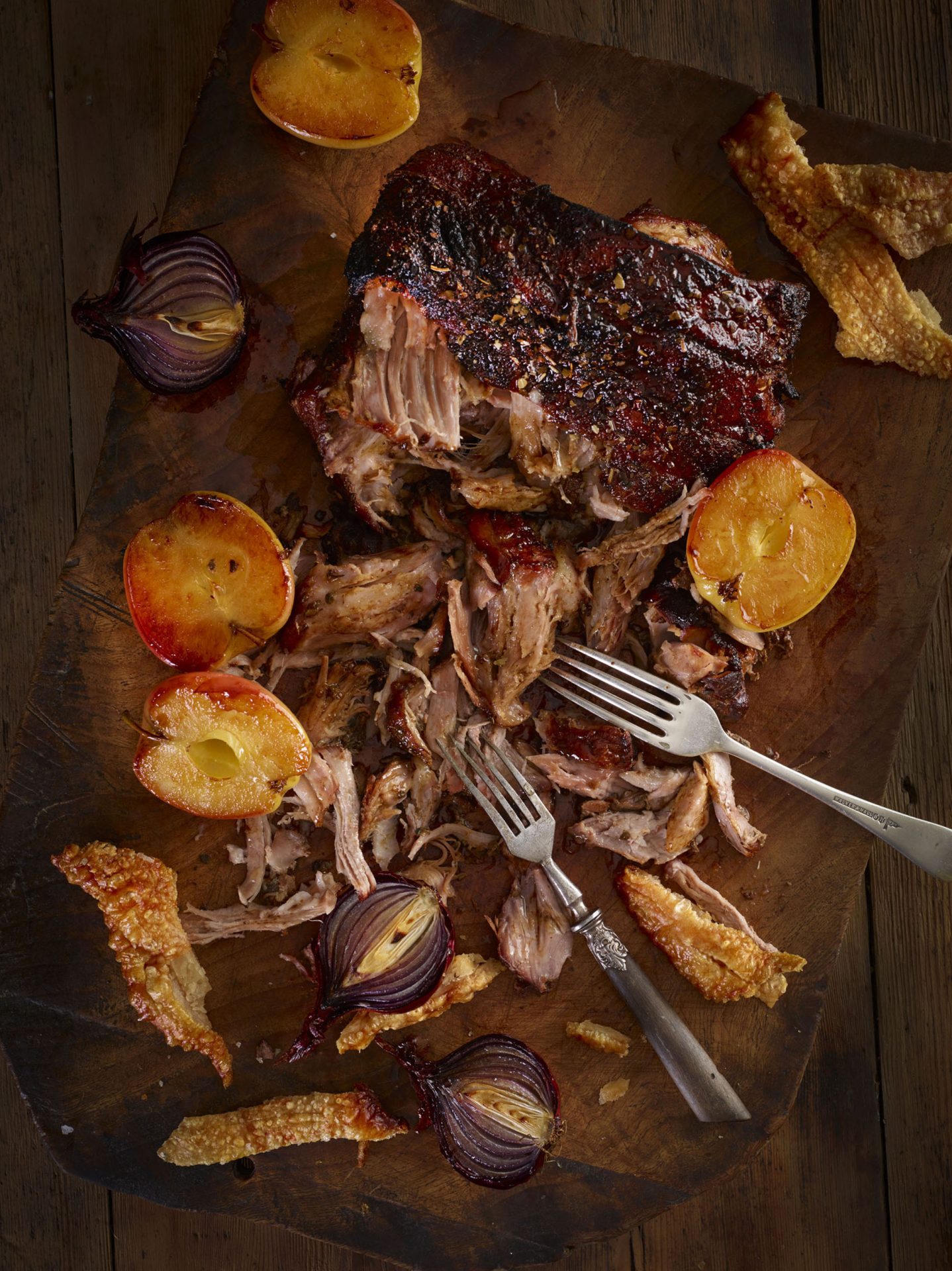 Pulled pork joint, some pulled, with apples and sage on a wooden board, with two forks