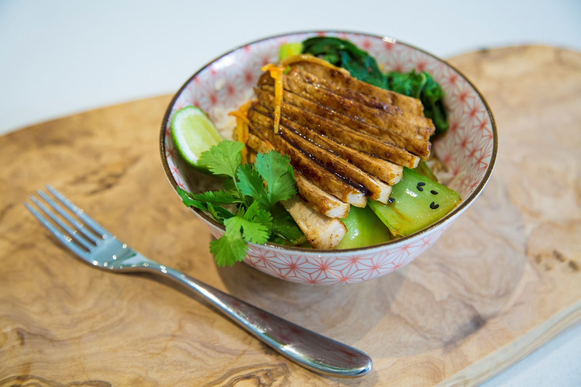 Sliced pork medallions on a bed of rice, served in a bowl with a fork on the side