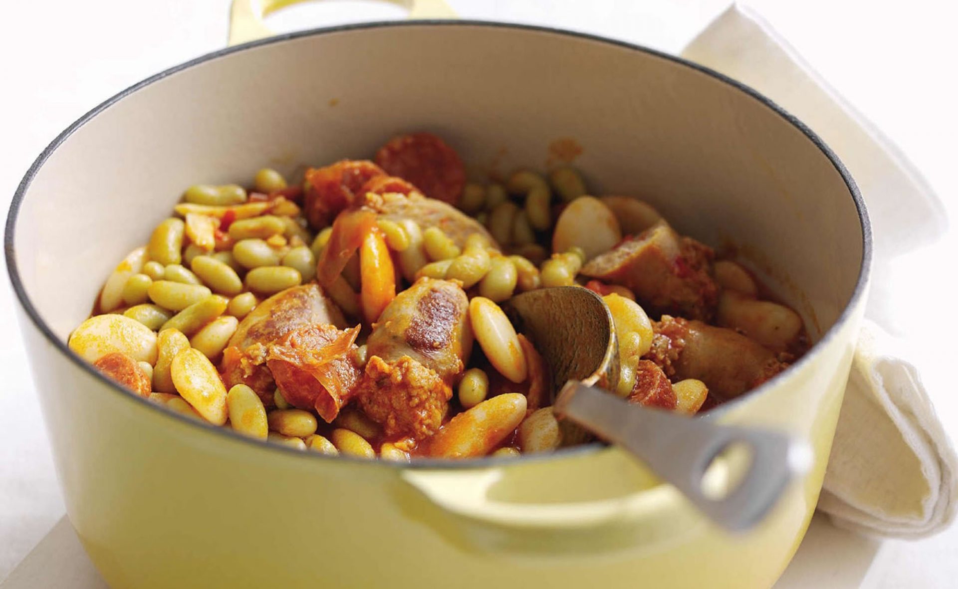 Sausage and bean cassoulet in a large white casserole dish with spoon