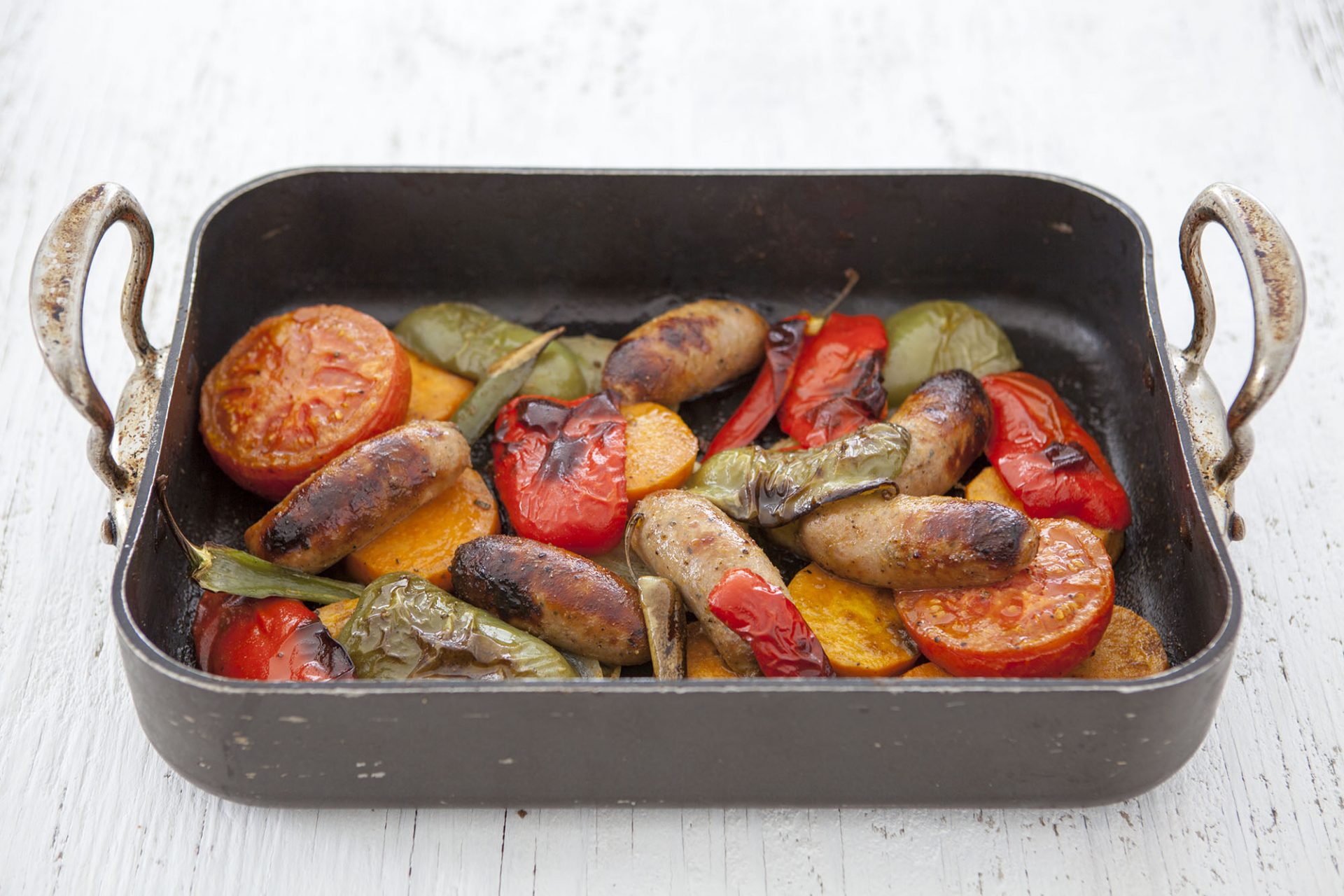 Sausage tray bake with green and red peppers served in a black baking tray