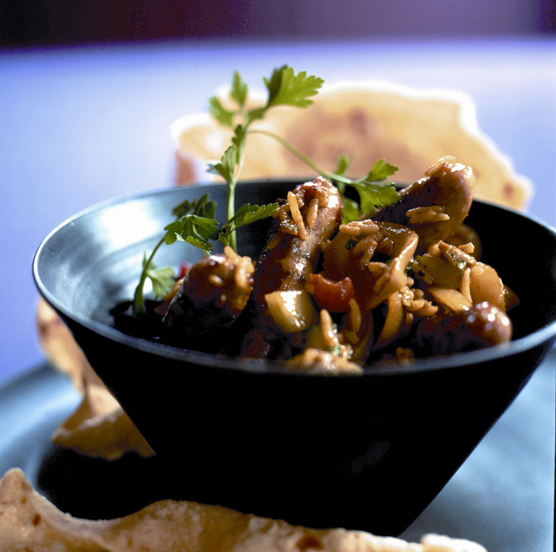 Sausage biryani in a black bowl with garnish