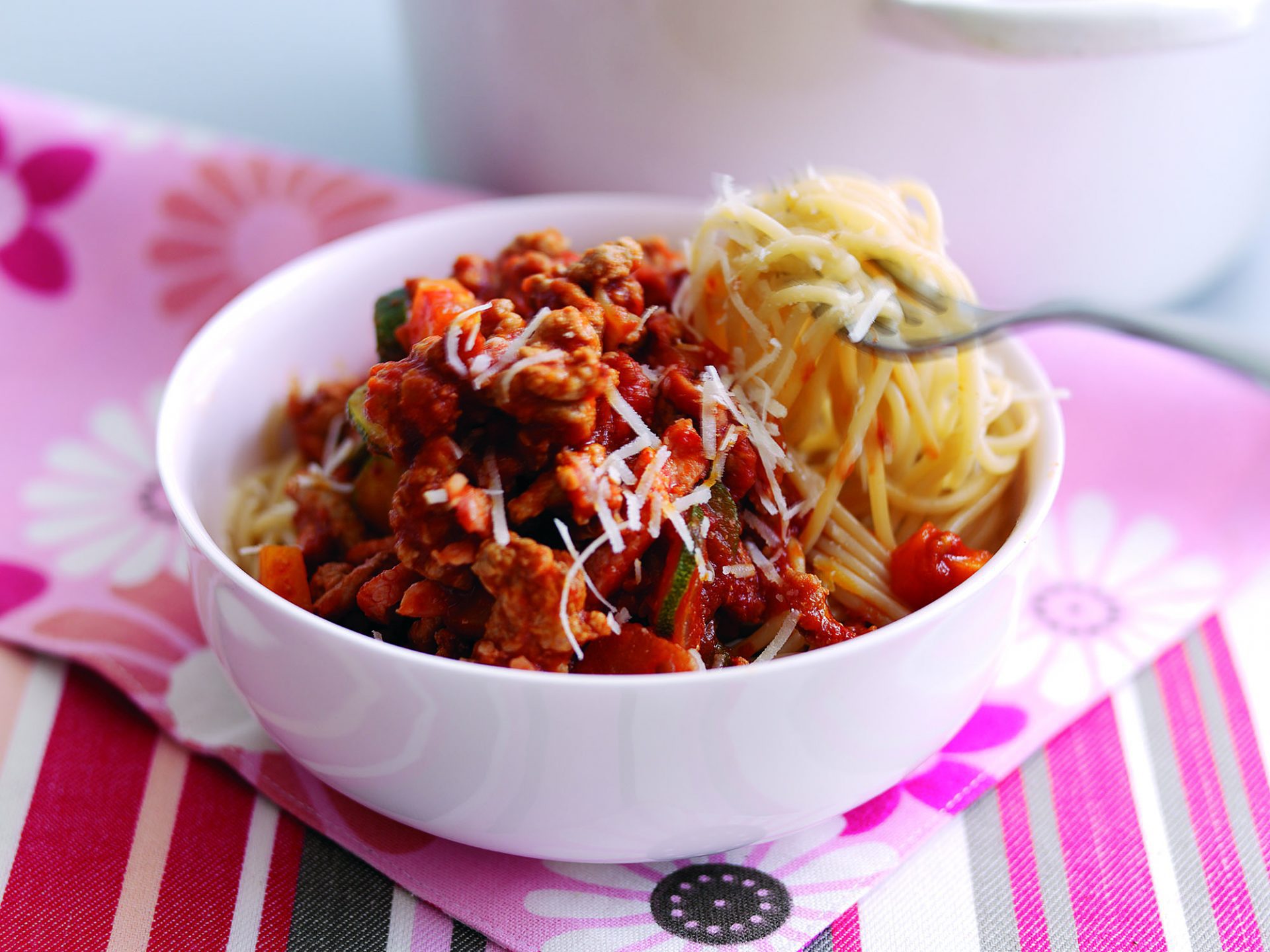 Sausage bolognese with spaghetti served in a white bowl with fork lifting up spaghetti