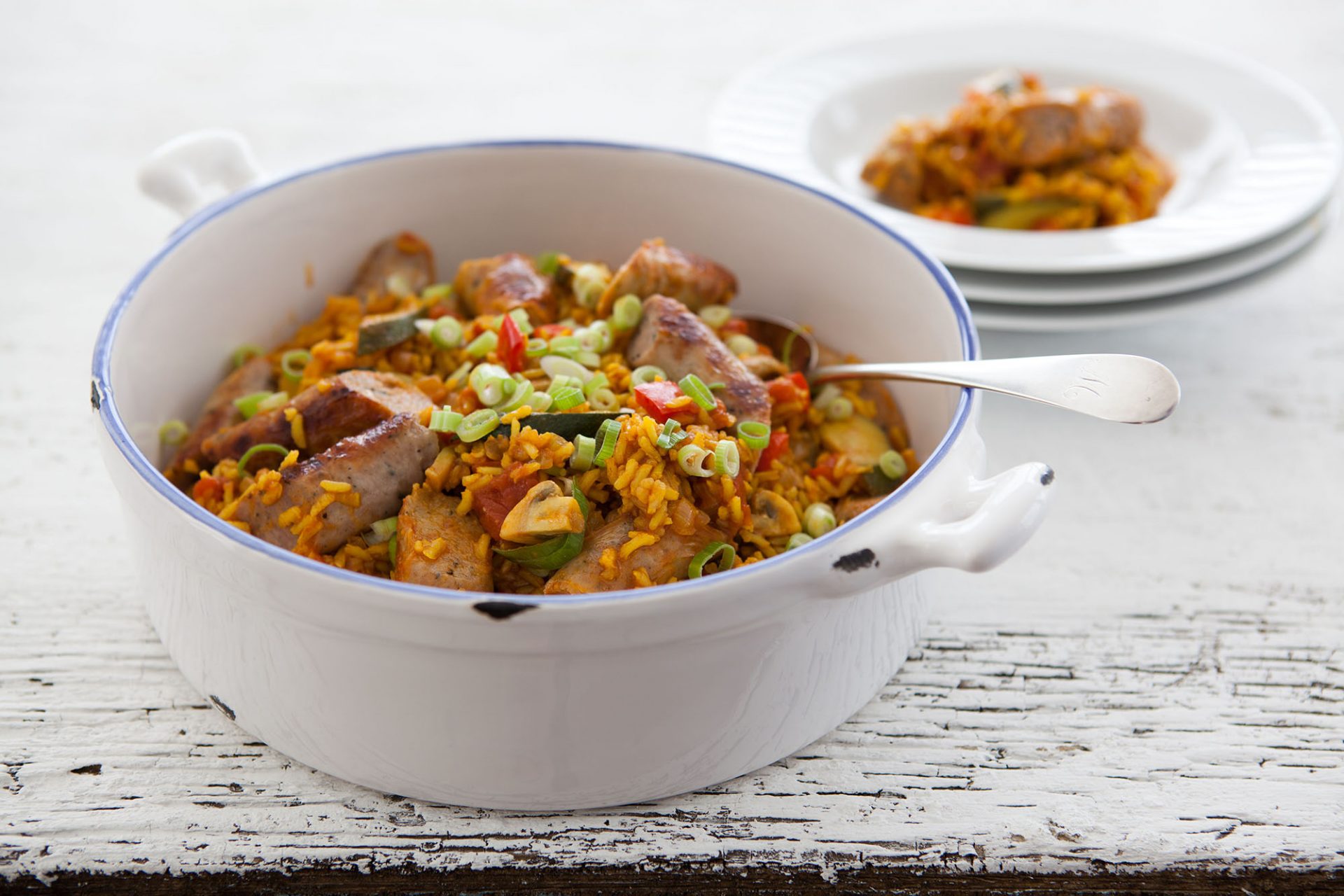 sausage jambalaya with spring onions in a white cooking pot with large serving spoon