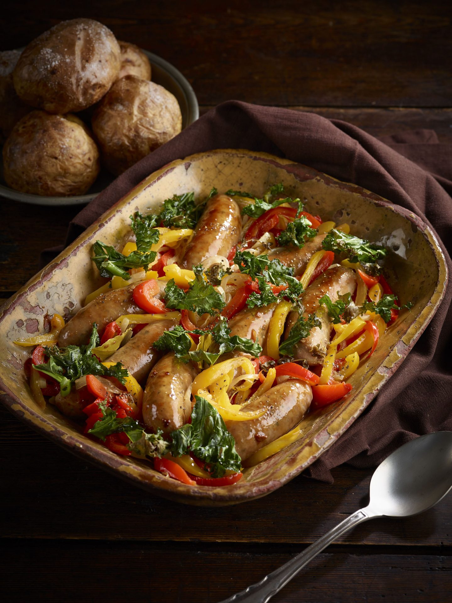 Large baking dish filled with stewed sausages, peppers and kale