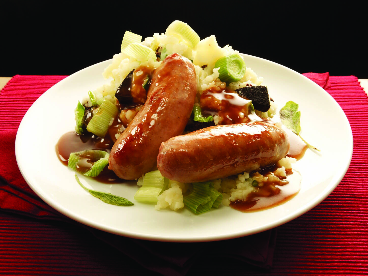 White plate with two sausages served on vegetables with sage and cider gravy