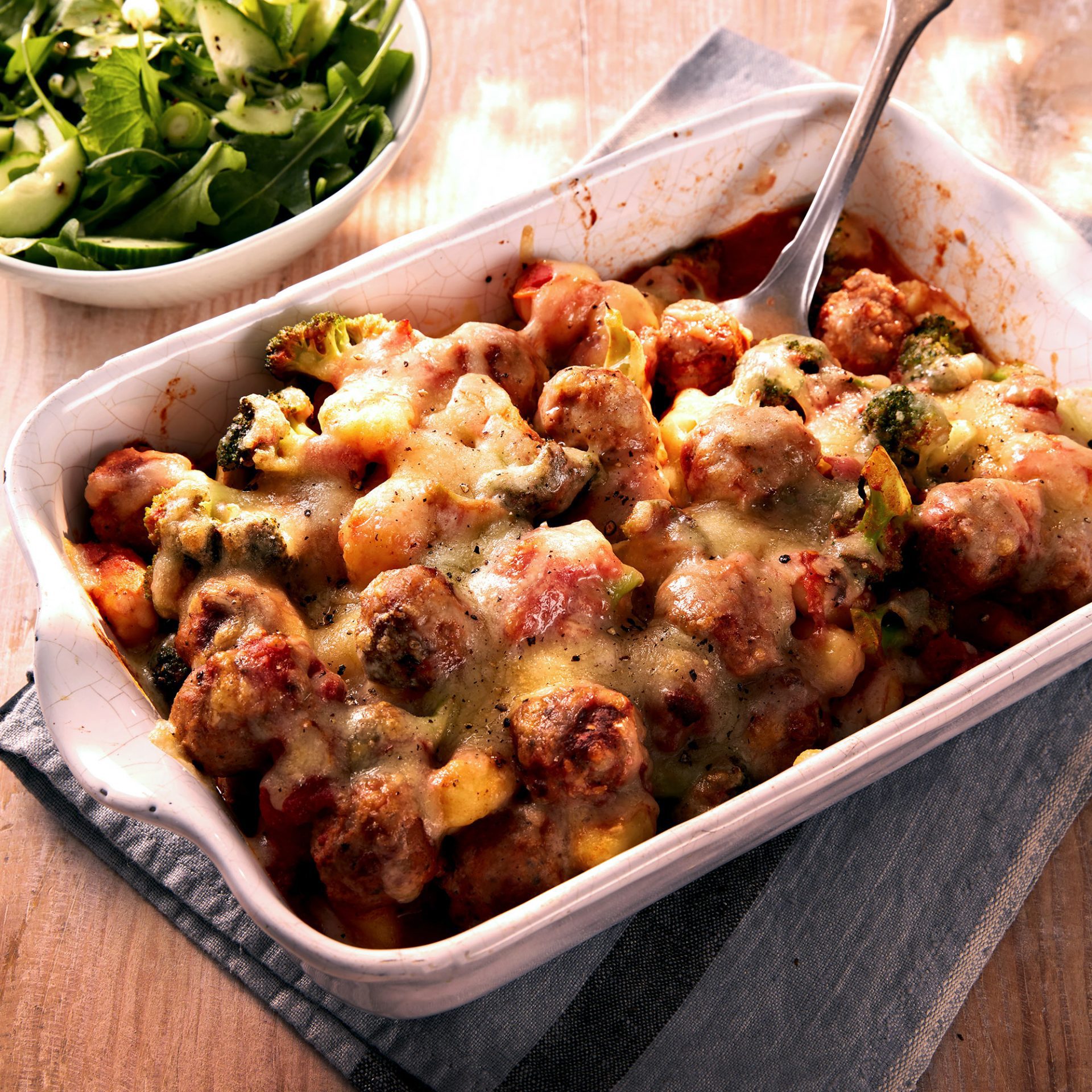 Large rectangle cooking dish filled with sausage gnocchi grain, with spoon in corner