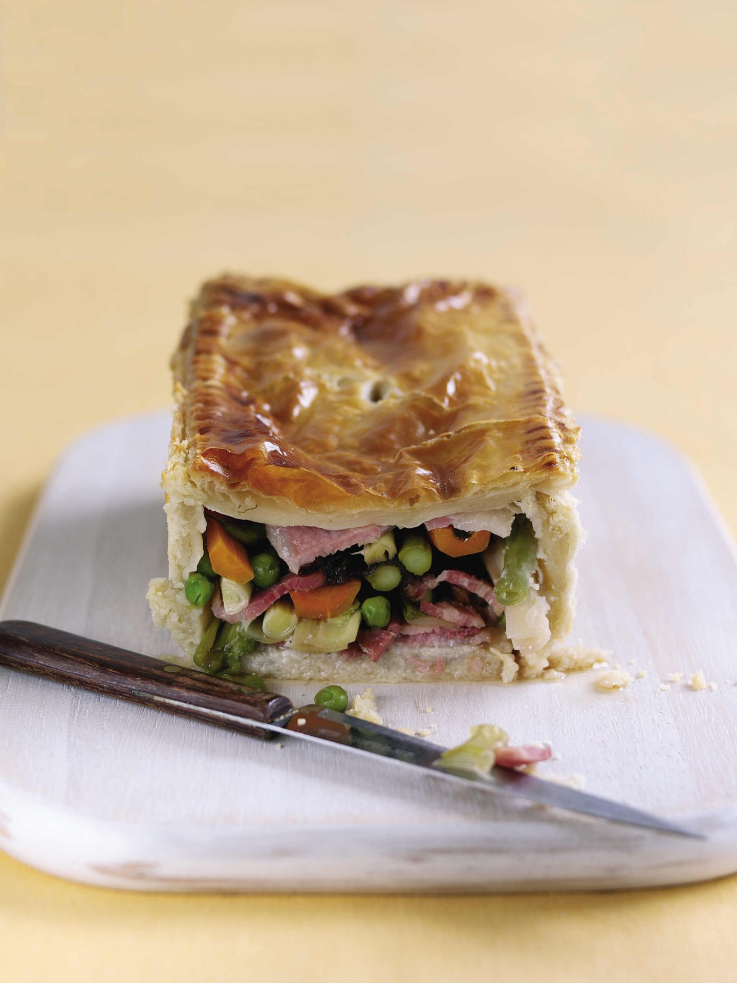 Sweet cured bacon pie with spring vegetables served on a white plate with knife