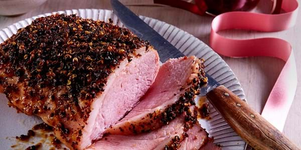 Roast gammon joint with Szechuan crust, some sliced, on a white platter with festive decor.