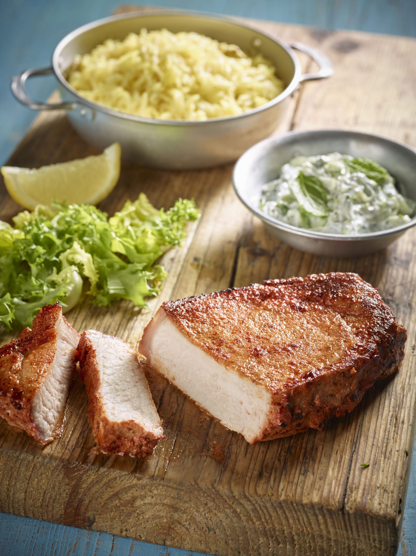 Pork steak, sliced, on a wooden chopping board with small side bowls in background