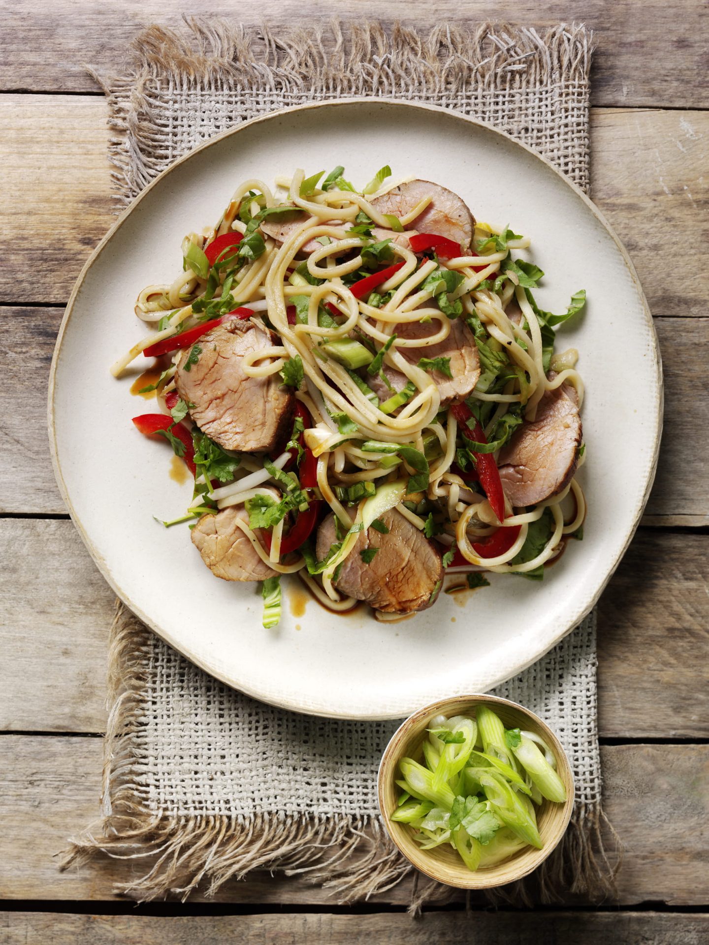 Sliced pork fillets on a noodle salad served on a white plate