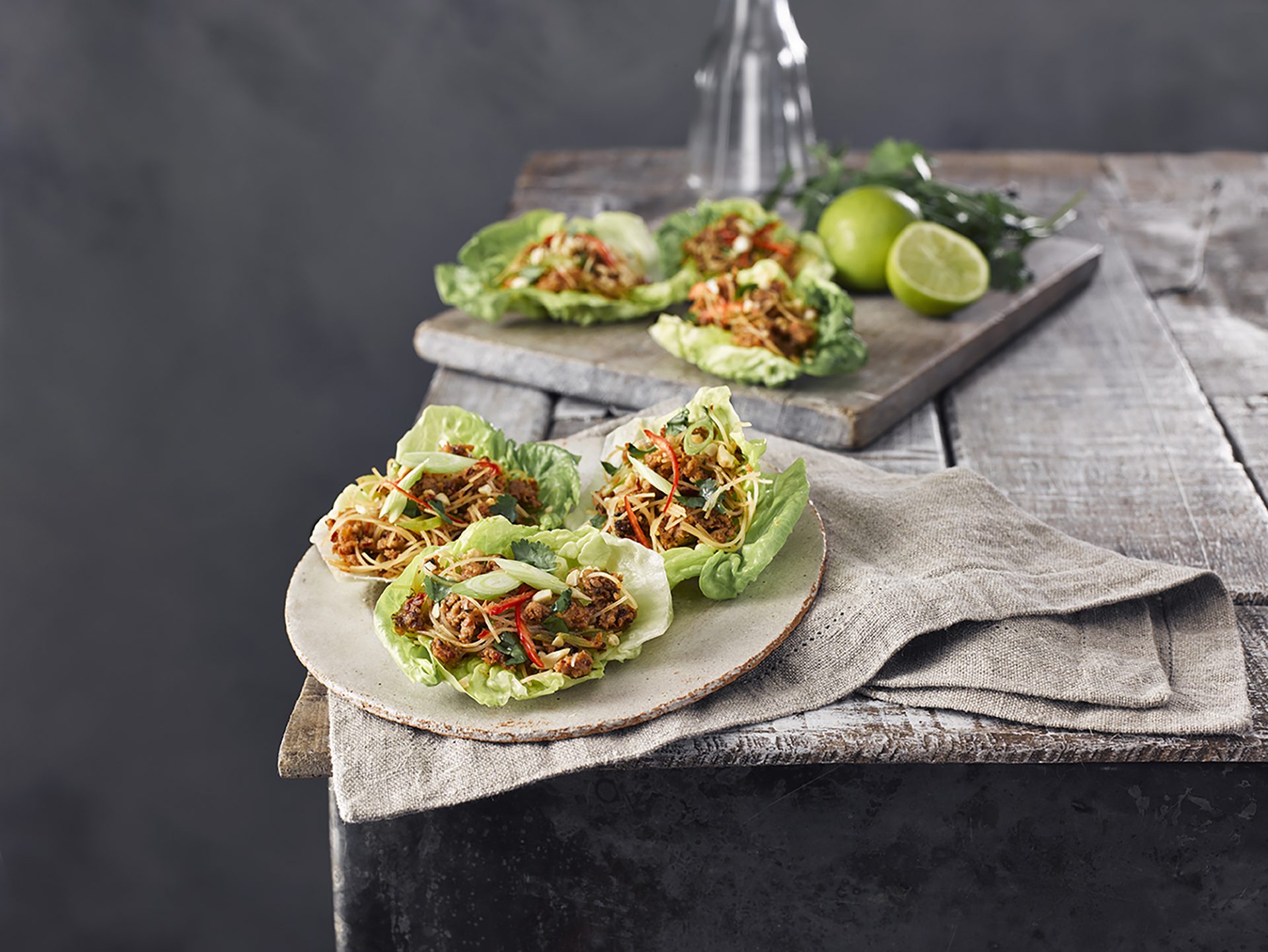 A group of 3 Thai sausage lettuce cups on a plate, with more in background on a board