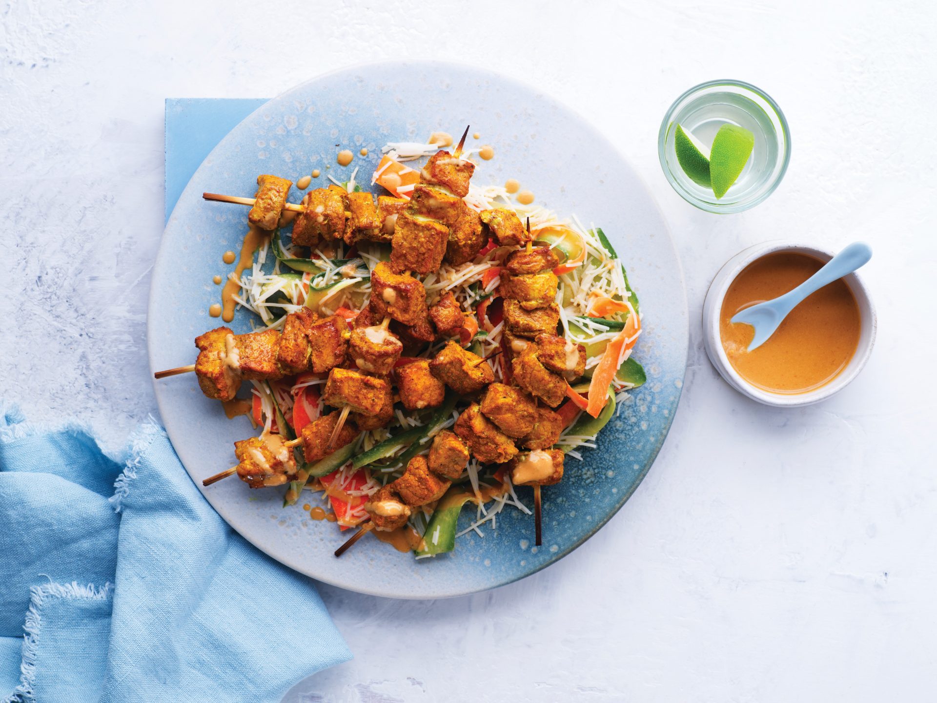 Pale blue plate with six pork satay skewers on a bed of salad.