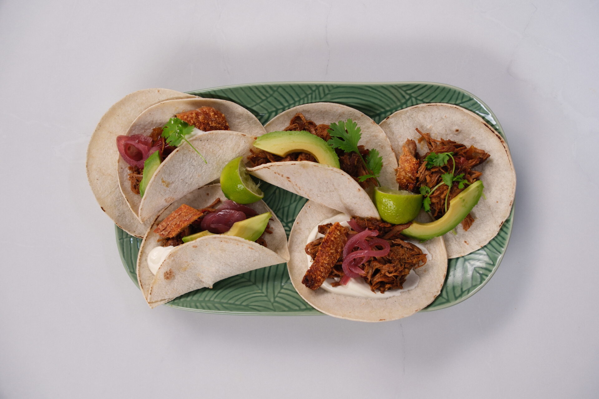 Pork shoulder carnitas in white tortilla wraps with crispy crackling and avocado