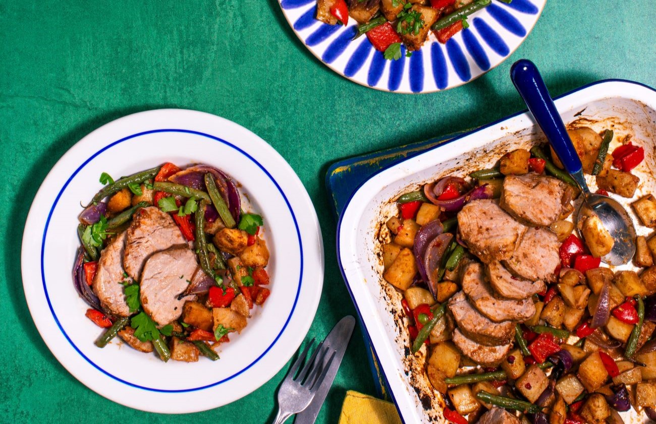 Pork Fillet Cajun Traybake with Vegetables in a large oven dish with spoon, and a serving on a white plate.