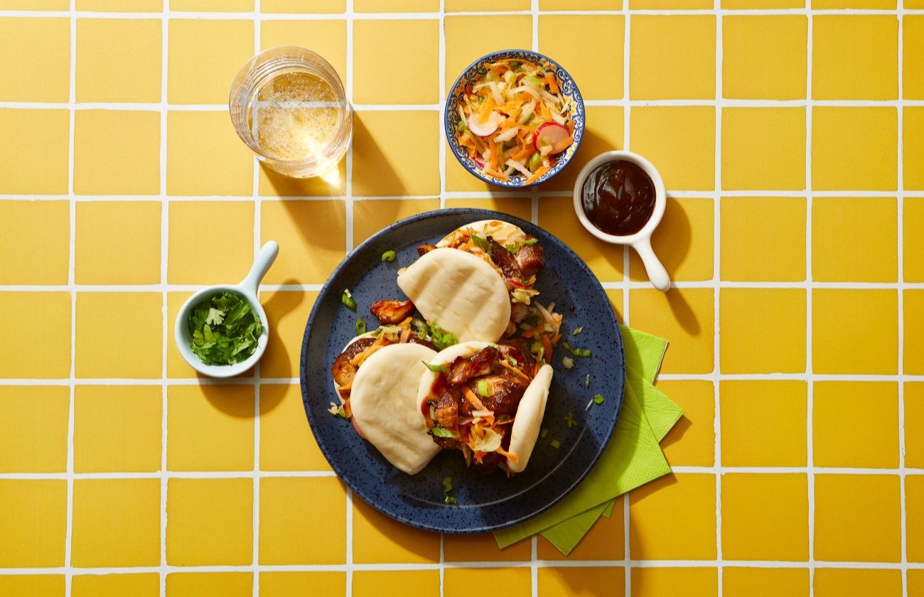 char sui pork belly bao buns on yellow tile background with serving suggestions