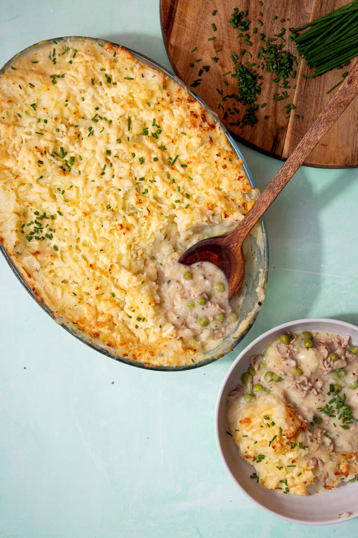 Pork cheese and potato pie in a large casserole dish with wooden serving spoon. Portion served in a bowl.