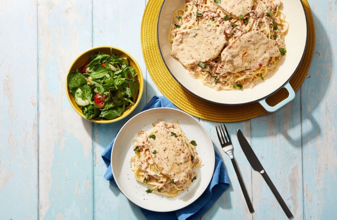 Marry Me Pork pasta served in a large white bowl with side salad and cutlery.