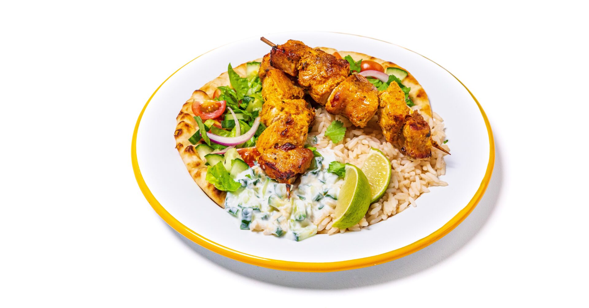 Tikka pork kebabs with rice, lime and sour cream on a white plate