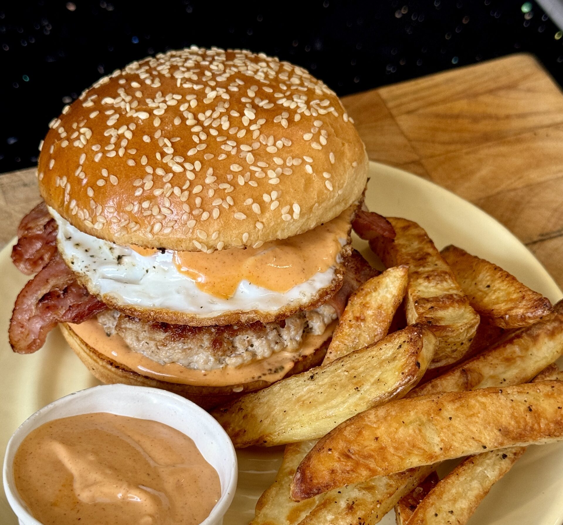 A pork breakfast burger on a plate with sauce and chips