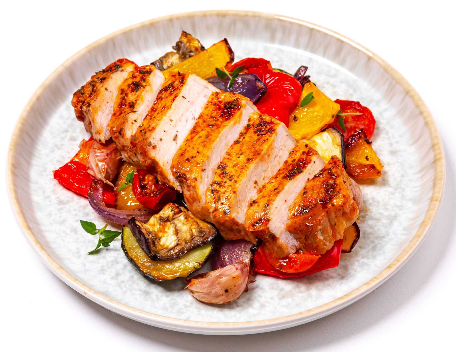 Air fried pork steak with peppers, courgettes and cherry tomatoes on a white plate